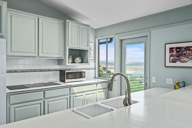 717 Mariner, Lakeway, TX 78734 - kitchen featuring stainless steel microwave, a sink, decorative backsplash, black electric stovetop, and vaulted ceiling