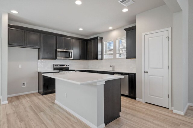 122 Elm Branch Trl, Taylor, TX 76574 - kitchen featuring appliances with stainless steel finishes, a kitchen island, backsplash, light countertops, and light wood-style floors