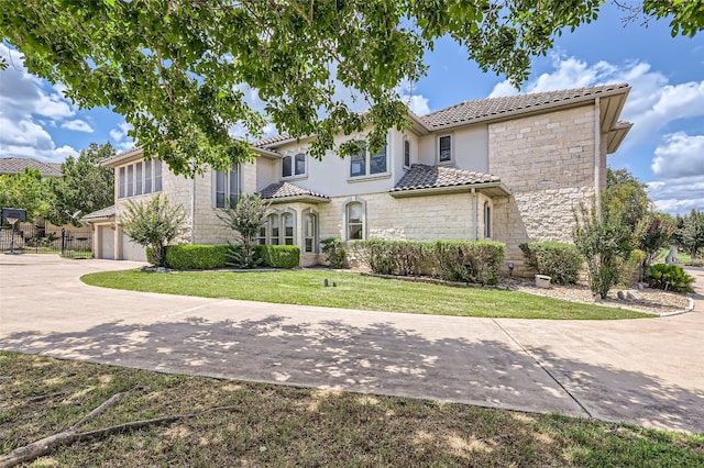 29 Tiburon Dr, The Hills, TX 78738 - mediterranean / spanish-style house featuring stone siding, a tiled roof, a front yard, concrete driveway, and an attached garage