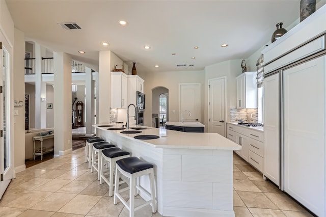 29 Tiburon Dr, The Hills, TX 78738 - kitchen with stainless steel appliances, a sink, arched walkways, a kitchen island with sink, and backsplash