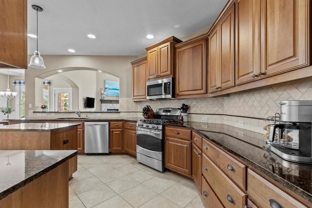 2700 Outlook Ridge Loop, Leander, TX 78641 - kitchen with stainless steel appliances, brown cabinetry, decorative backsplash, dark stone counters, and recessed lighting