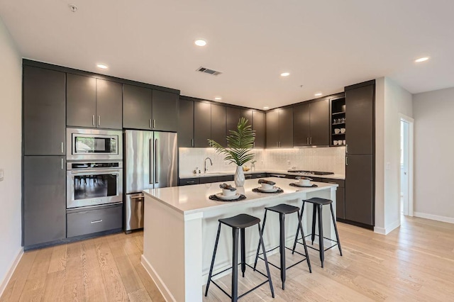900 S 1st St Unit 212, Austin, TX 78704 - kitchen with appliances with stainless steel finishes, open shelves, a kitchen breakfast bar, tasteful backsplash, and light wood-type flooring