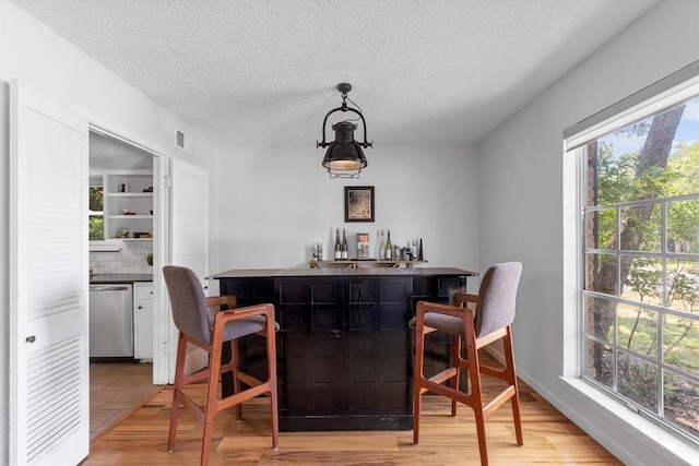 3104 Rexford Dr, Austin, TX 78723 - indoor wet bar with stainless steel dishwasher, a textured ceiling, light wood finished floors, hanging light fixtures, and backsplash