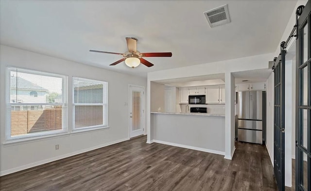1709 Greenlawn Blvd, Round Rock, TX 78664 - kitchen with a barn door, freestanding refrigerator, black microwave, dark wood-style floors, and light countertops