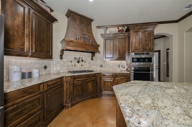 2543 Fm 975, Caldwell, TX 77836 - kitchen featuring custom exhaust hood, arched walkways, tasteful backsplash, light stone countertops, and dark brown cabinets