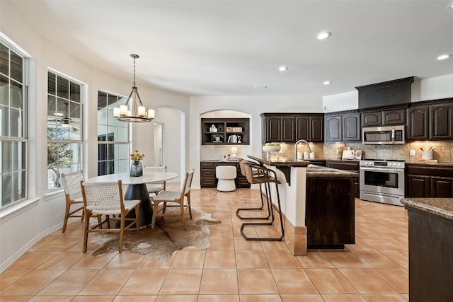8311 Sumner Ct, Austin, TX 78733 - kitchen with appliances with stainless steel finishes, a kitchen breakfast bar, backsplash, dark brown cabinets, and a chandelier