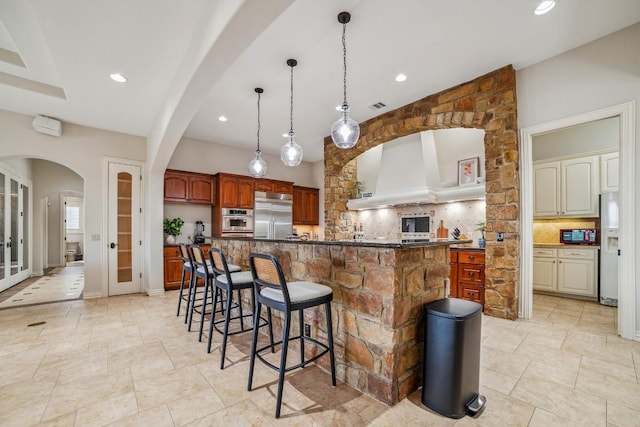 12529 Verandah Ct, Austin, TX 78726 - kitchen featuring appliances with stainless steel finishes, decorative backsplash, arched walkways, a breakfast bar, and a spacious island