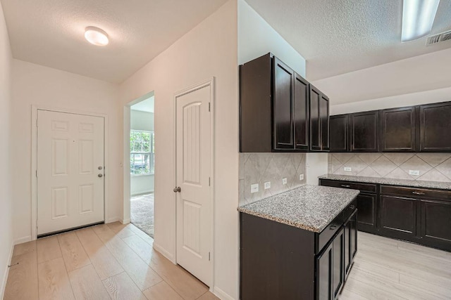 14309 Deaf Smith Blvd, Austin, TX 78725 - kitchen featuring light wood-style floors, backsplash, a textured ceiling, light stone counters, and baseboards