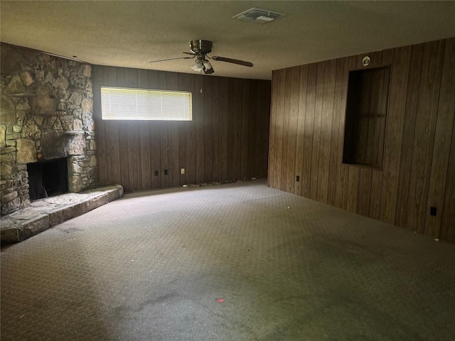 200 W Odell St, Austin, TX 78752 - unfurnished living room with carpet, ceiling fan, wood walls, a stone fireplace, and a textured ceiling
