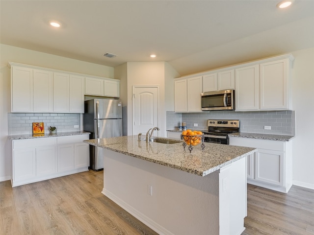 102 Sandpiper Dr, Bastrop, TX 78602 - kitchen with stainless steel appliances, decorative backsplash, white cabinetry, a kitchen island with sink, and light stone counters