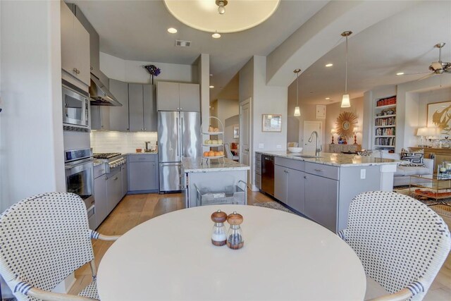 8200 SW Pkwy Unit 721, Austin, TX 78735 - kitchen with appliances with stainless steel finishes, gray cabinets, an island with sink, backsplash, and light wood finished floors