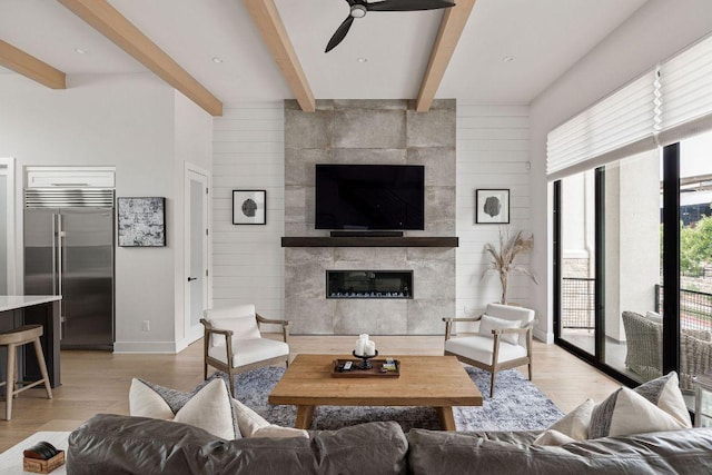 13410 Galleria Cir, Austin, TX 78738 - living room featuring light wood-type flooring, a tiled fireplace, ceiling fan, beamed ceiling, and baseboards