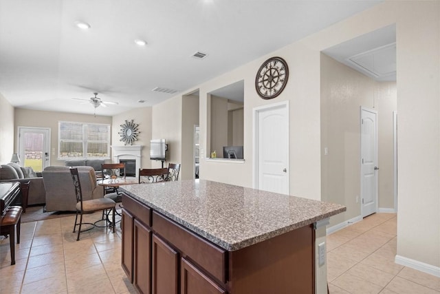 1608 Torre St, Leander, TX 78641 - kitchen featuring a ceiling fan, light tile patterned flooring, a glass covered fireplace, a kitchen island, and light countertops
