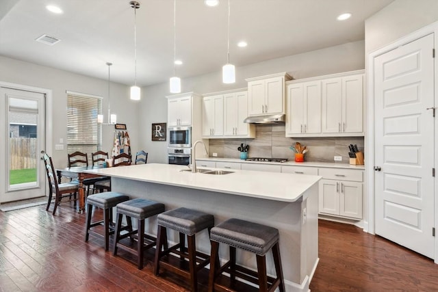 1005 Hezekiah Ln, Leander, TX 78641 - kitchen with stainless steel appliances, under cabinet range hood, dark wood-style flooring, decorative backsplash, and a breakfast bar