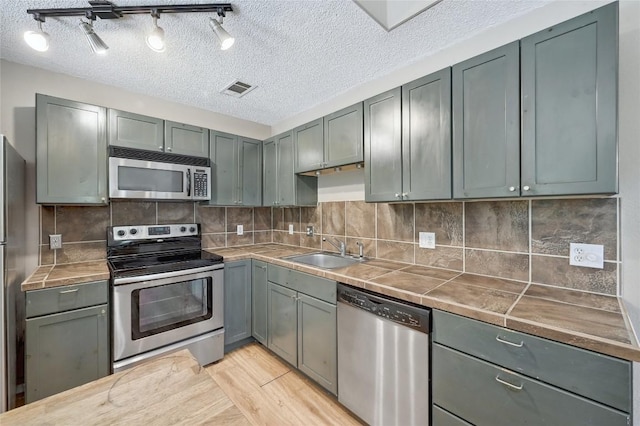 907 The High Rd, Austin, TX 78746 - kitchen with stainless steel appliances, a sink, a textured ceiling, light wood finished floors, and tile countertops