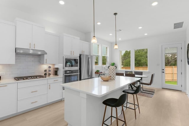2705 Sage Ranch Dr Unit 2, Leander, TX 78641 - kitchen featuring appliances with stainless steel finishes, under cabinet range hood, light wood-style flooring, decorative backsplash, and a center island