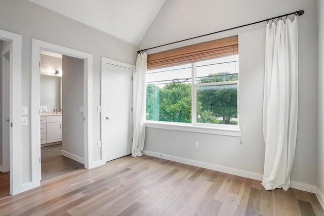 4020 Airport Blvd Unit 9, Austin, TX 78722 - unfurnished bedroom featuring light wood finished floors, vaulted ceiling, baseboards, ensuite bathroom, and a sink