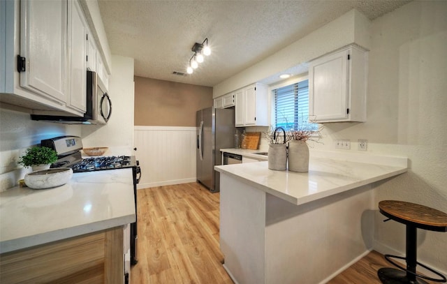 615 Twin Oak Trl, Cedar Park, TX 78613 - kitchen featuring appliances with stainless steel finishes, a peninsula, white cabinets, a breakfast bar, and a wainscoted wall