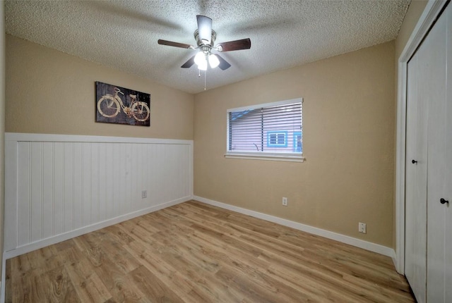 615 Twin Oak Trl, Cedar Park, TX 78613 - unfurnished bedroom with wood finished floors, a textured ceiling, a closet, a wainscoted wall, and a ceiling fan