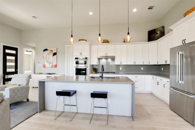 105 Golden Eagle, Horseshoe Bay, TX 78657 - kitchen with appliances with stainless steel finishes, under cabinet range hood, a breakfast bar area, an island with sink, and white cabinetry