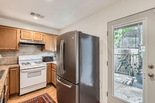 1411 Gracy Farms Ln Unit 113, Austin, TX 78758 - kitchen featuring freestanding refrigerator, white gas range oven, exhaust hood, light wood-type flooring, and decorative backsplash