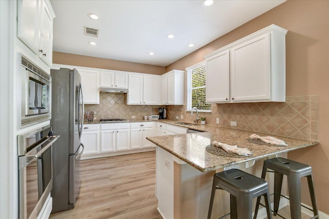 19420 Brue St, Pflugerville, TX 78660 - kitchen with appliances with stainless steel finishes, a peninsula, light wood-style floors, white cabinets, and recessed lighting
