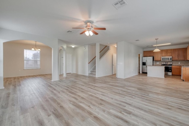 9104 China Rose Dr, Austin, TX 78724 - unfurnished living room with arched walkways, light wood-type flooring, a chandelier, a ceiling fan, and stairway