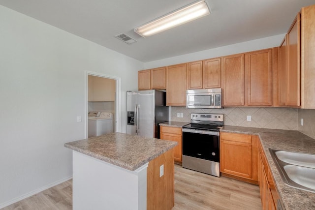 9104 China Rose Dr, Austin, TX 78724 - kitchen with appliances with stainless steel finishes, separate washer and dryer, tasteful backsplash, light wood-style flooring, and a center island