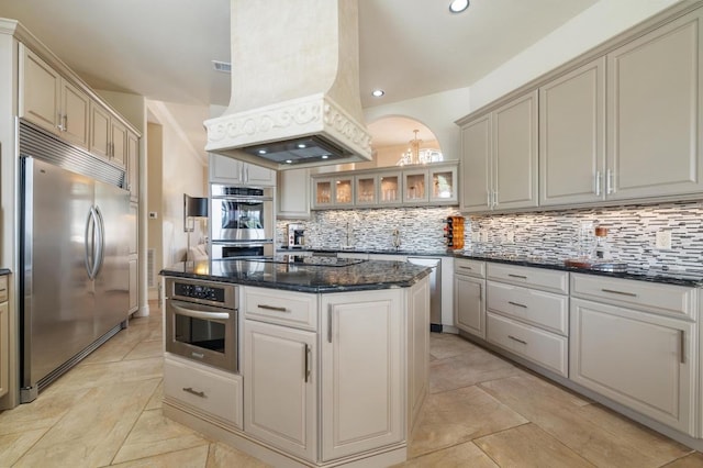 20503 Hoover Cv, Lago Vista, TX 78645 - kitchen featuring stainless steel appliances, custom exhaust hood, decorative backsplash, a center island, and glass insert cabinets