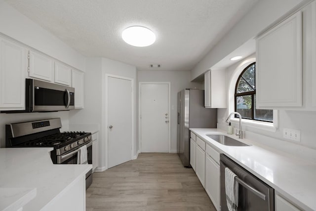 8407 Mount Shasta Cv, Round Rock, TX 78681 - kitchen featuring stainless steel appliances, a sink, white cabinets, a textured ceiling, and light wood-style floors