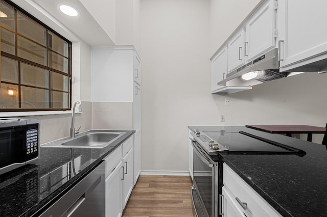 1908 San Antonio St Unit 313, Austin, TX 78705 - kitchen featuring stainless steel appliances, under cabinet range hood, light wood-style floors, white cabinetry, and dark stone counters