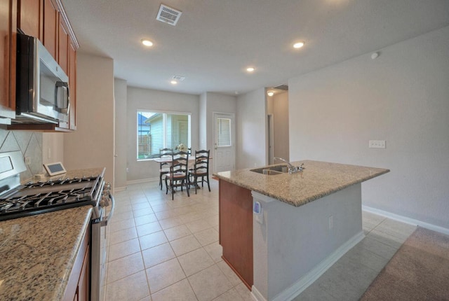 211 S Timber Brook Dr, Hutto, TX 78634 - kitchen featuring appliances with stainless steel finishes, brown cabinets, a kitchen island with sink, light stone counters, and recessed lighting