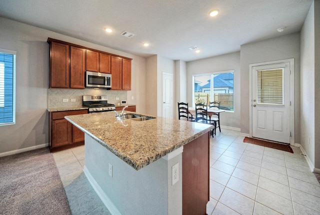 211 S Timber Brook Dr, Hutto, TX 78634 - kitchen featuring stainless steel appliances, light tile patterned floors, light stone counters, an island with sink, and plenty of natural light