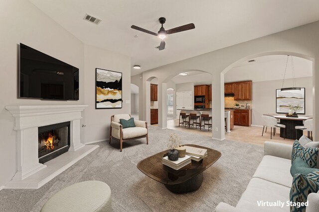 1129 Wigwam Dr, Leander, TX 78641 - living room featuring a ceiling fan, light carpet, arched walkways, and a lit fireplace