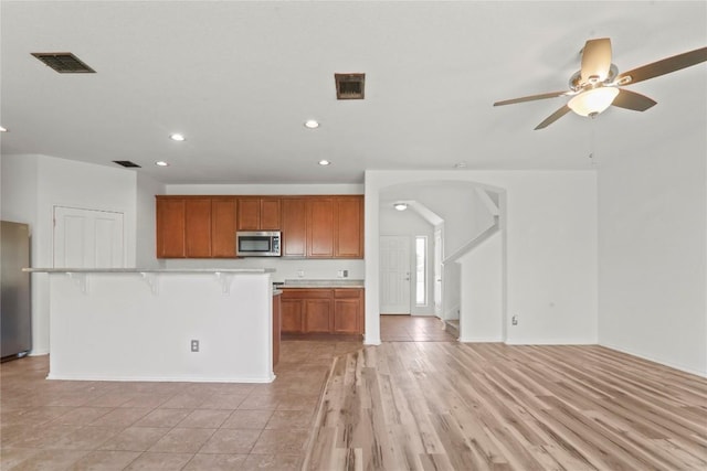 232 Wells Bnd, Hutto, TX 78634 - kitchen with appliances with stainless steel finishes, arched walkways, recessed lighting, light countertops, and brown cabinets