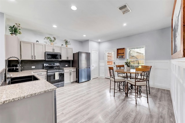 107 Denton Dr, Hutto, TX 78634 - kitchen featuring appliances with stainless steel finishes, decorative backsplash, light stone counters, light wood finished floors, and a wainscoted wall