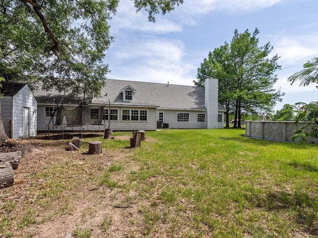 2939 Jeffcote Rd, Conroe, TX 77303 - rear view of house with a trampoline, a lawn, a chimney, an outdoor pool, and roof with shingles