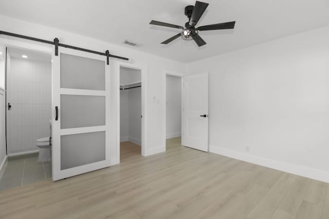 1509 Parkview Ln, San Marcos, TX 78666 - unfurnished bedroom with a barn door, a walk in closet, light wood finished floors, and baseboards