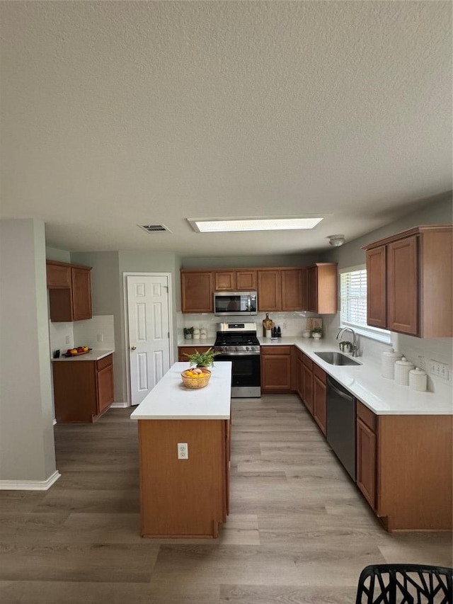 10301 Beard Ave, Austin, TX 78748 - kitchen with appliances with stainless steel finishes, a sink, light wood-style floors, a textured ceiling, and a center island