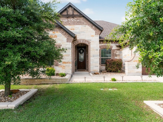 116 Waterloo Cv, Georgetown, TX 78628 - view of front facade with stone siding, a front yard, roof with shingles, and brick siding