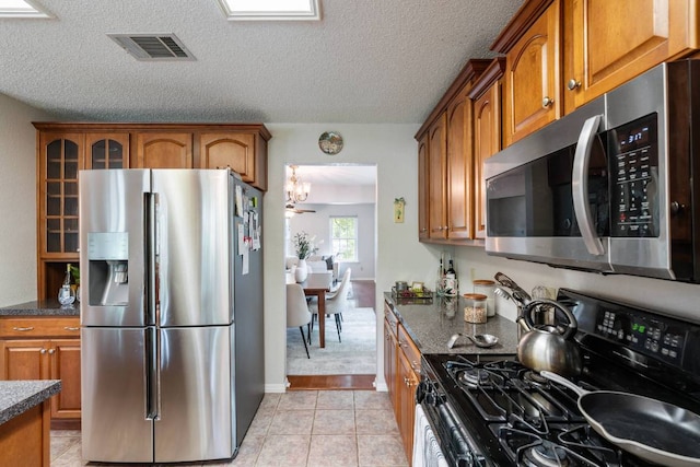 1202 Tremont Dr, Cedar Park, TX 78613 - kitchen featuring stainless steel appliances, brown cabinets, light tile patterned flooring, glass insert cabinets, and a chandelier