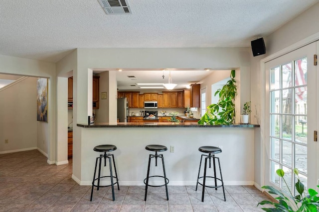 1202 Tremont Dr, Cedar Park, TX 78613 - kitchen with stainless steel appliances, brown cabinetry, healthy amount of natural light, a kitchen bar, and a textured ceiling
