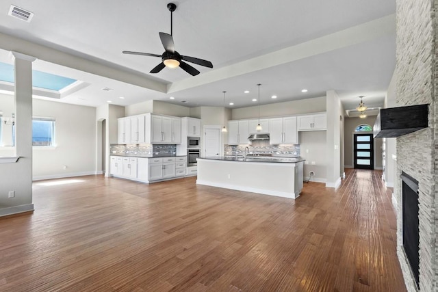 18716 Waltz Ct, Austin, TX 78738 - unfurnished living room with ceiling fan, a tray ceiling, a stone fireplace, wood finished floors, and baseboards
