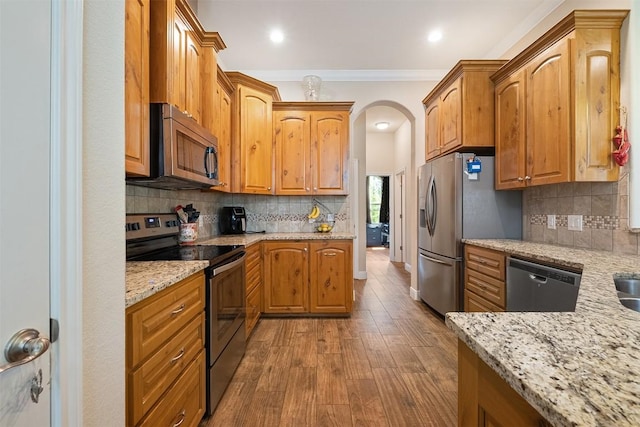 108 Kaliu Ct, Bastrop, TX 78602 - kitchen with stainless steel appliances, light stone counters, arched walkways, dark wood-type flooring, and crown molding