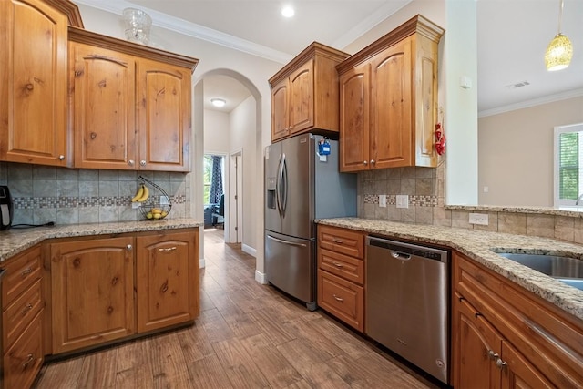 108 Kaliu Ct, Bastrop, TX 78602 - kitchen featuring appliances with stainless steel finishes, light stone counters, arched walkways, wood finished floors, and decorative backsplash