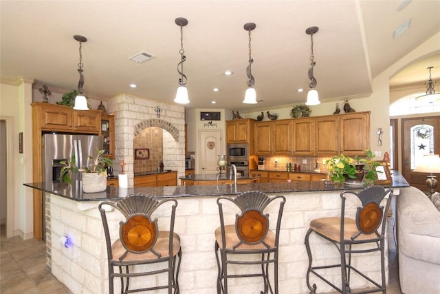 1265 Mourning Dove Ct, Salado, TX 76571 - kitchen featuring stainless steel appliances, brown cabinetry, arched walkways, backsplash, and a breakfast bar