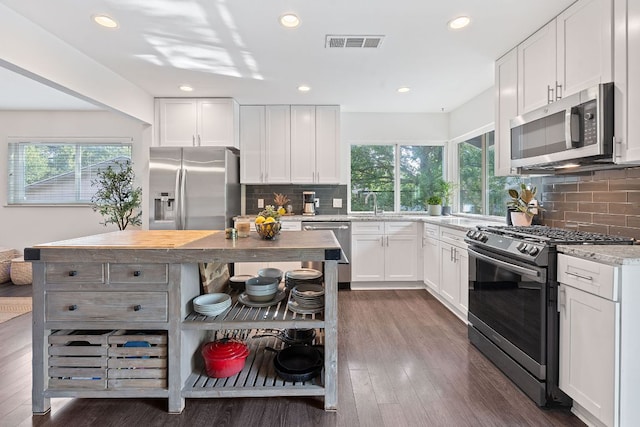 6610 Greensboro Dr, Austin, TX 78723 - kitchen with appliances with stainless steel finishes, backsplash, white cabinetry, dark wood-style floors, and recessed lighting