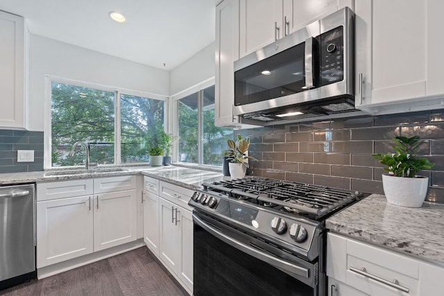 6610 Greensboro Dr, Austin, TX 78723 - kitchen featuring appliances with stainless steel finishes, white cabinetry, light stone countertops, dark wood-style flooring, and decorative backsplash