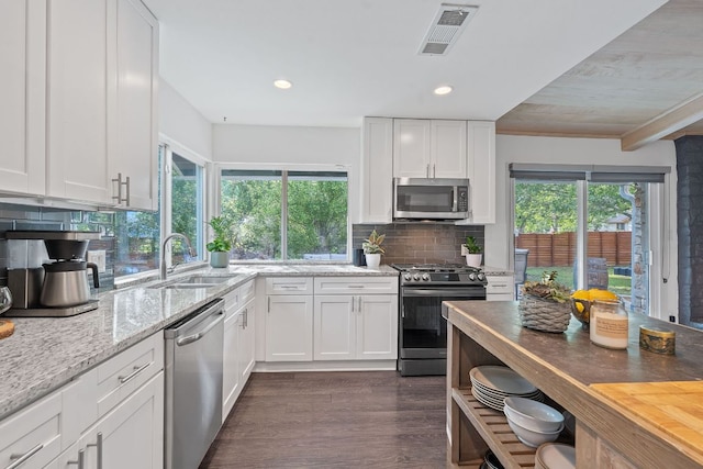 6610 Greensboro Dr, Austin, TX 78723 - kitchen with appliances with stainless steel finishes, light stone countertops, white cabinets, decorative backsplash, and plenty of natural light