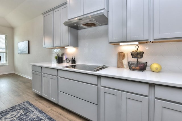 311 Westfield St, Hutto, TX 78634 - kitchen featuring gray cabinetry, black electric cooktop, under cabinet range hood, light wood finished floors, and backsplash